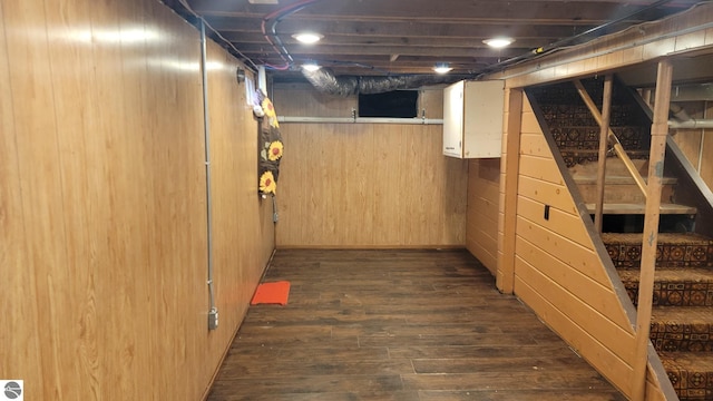 unfinished basement featuring stairs, wood walls, and dark wood finished floors