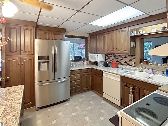 kitchen featuring white appliances, backsplash, a paneled ceiling, and a sink