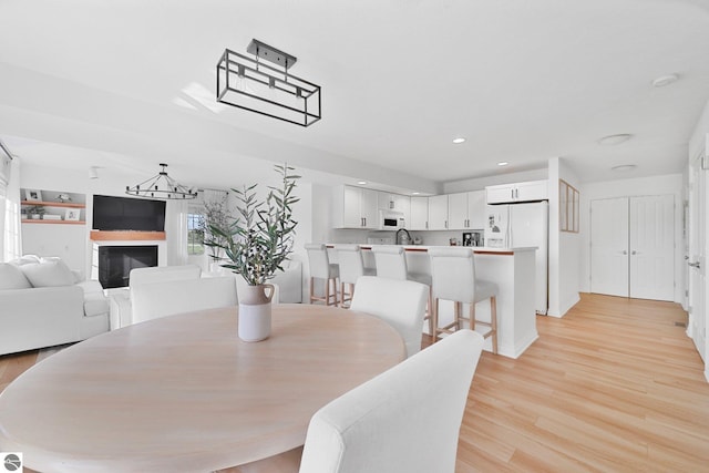 dining room with a glass covered fireplace, recessed lighting, light wood-style flooring, and a notable chandelier