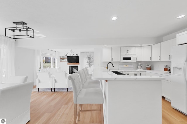 kitchen with white appliances, white cabinets, a sink, and light wood-style floors