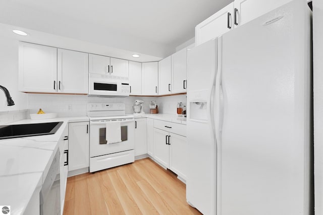 kitchen featuring white cabinets, a sink, white appliances, recessed lighting, and light wood-type flooring
