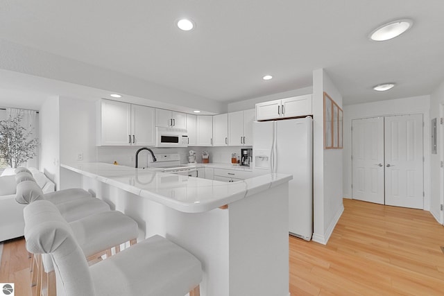kitchen with a kitchen breakfast bar, white cabinets, a peninsula, recessed lighting, and white appliances