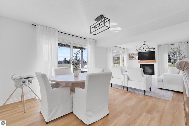 dining area with a glass covered fireplace, baseboards, light wood finished floors, and a chandelier