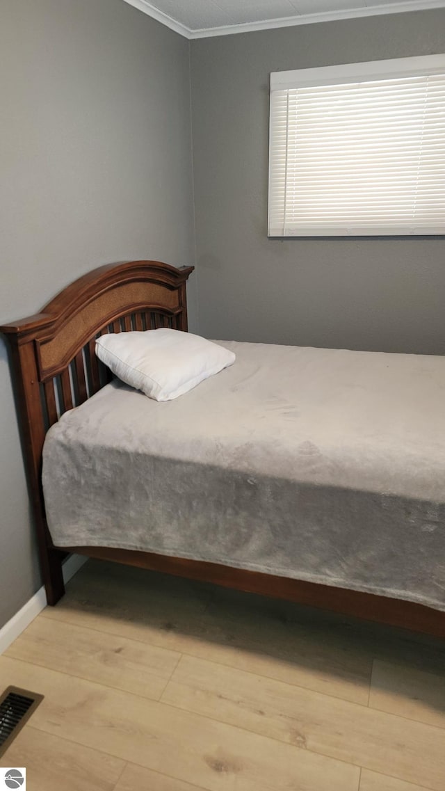 bedroom featuring visible vents, ornamental molding, and wood finished floors
