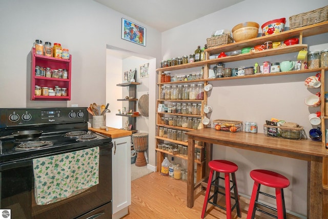 kitchen featuring open shelves, wooden counters, a kitchen bar, black range with electric stovetop, and light wood-style flooring