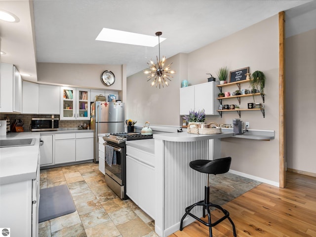 431 E Bittner Ave, Reed City, MI 49618 - kitchen featuring appliances with stainless steel finishes, tasteful backsplash, white cabinets, lofted ceiling with skylight, and a breakfast bar