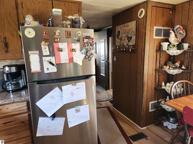 kitchen with visible vents, freestanding refrigerator, wood finished floors, and brown cabinets