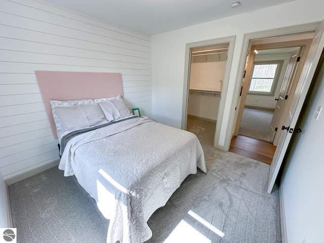 carpeted bedroom with baseboards, wood walls, and a walk in closet