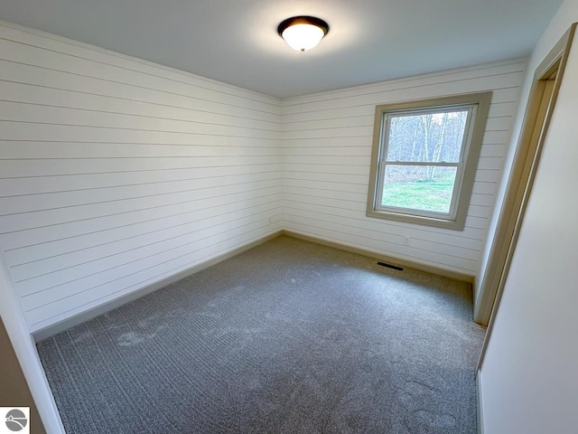 carpeted empty room featuring visible vents and wooden walls