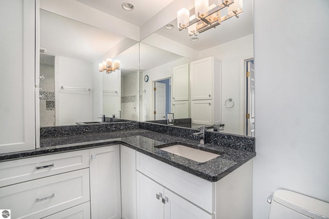 bathroom featuring double vanity, a tile shower, a sink, toilet, and an inviting chandelier