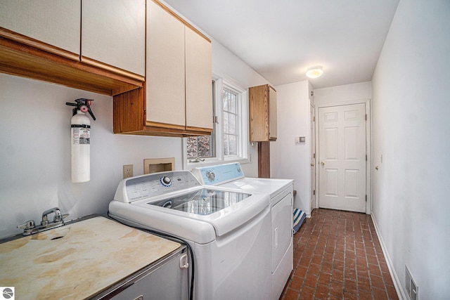 clothes washing area featuring visible vents, cabinet space, baseboards, brick floor, and washer and clothes dryer