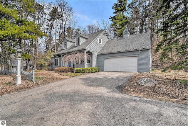 cape cod-style house featuring an attached garage, a shingled roof, aphalt driveway, and a chimney