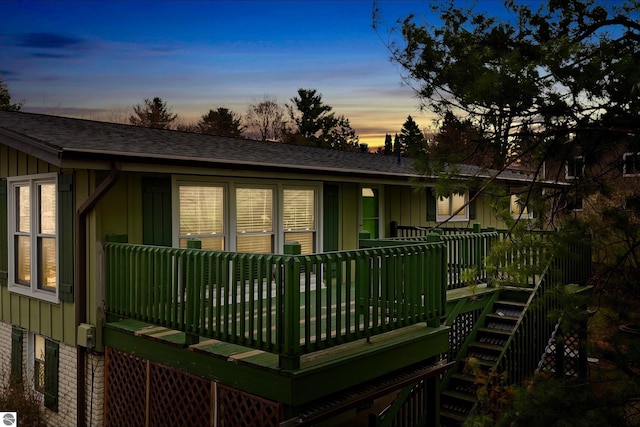 back of property at dusk featuring stairs, a shingled roof, board and batten siding, and a wooden deck