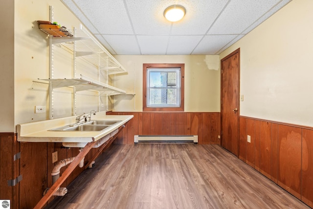 interior space featuring wood finished floors, a baseboard heating unit, a sink, and a wainscoted wall