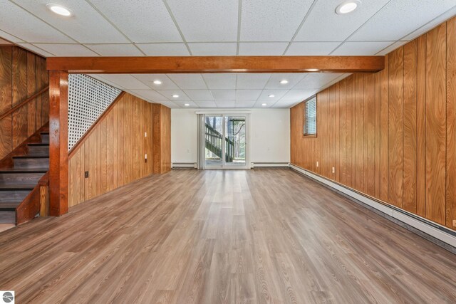 unfurnished living room featuring wooden walls, baseboard heating, stairs, wood finished floors, and a baseboard heating unit