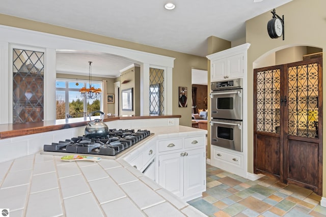 kitchen featuring stone finish floor, tile countertops, white cabinetry, a chandelier, and appliances with stainless steel finishes