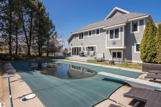 back of house with roof with shingles, a wooden deck, a covered pool, and a patio area
