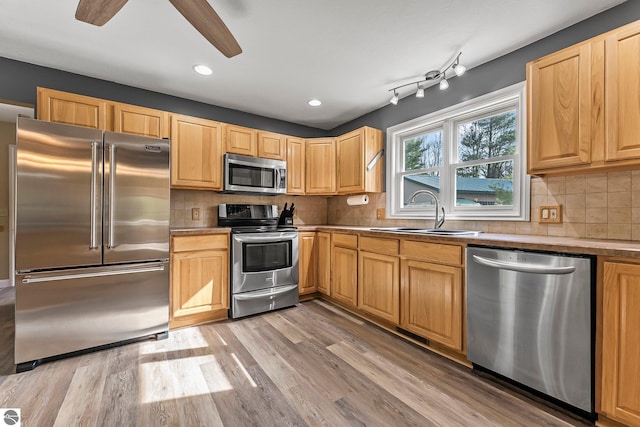 kitchen featuring a sink, backsplash, stainless steel appliances, and light wood finished floors