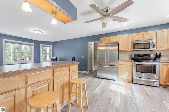 kitchen with a breakfast bar area, backsplash, visible vents, light brown cabinetry, and stainless steel appliances