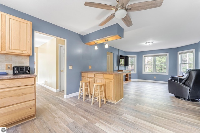 kitchen with light brown cabinetry, a breakfast bar, light wood-style floors, open floor plan, and baseboards