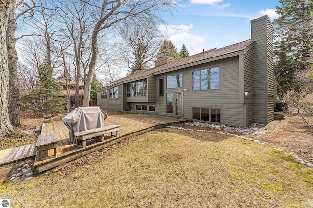 back of house featuring a lawn, a shingled roof, a chimney, and a deck