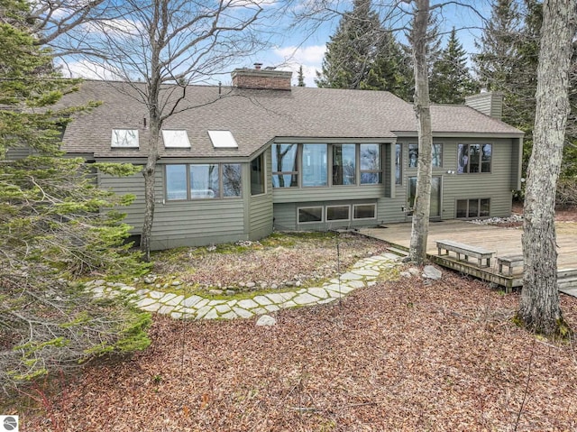 back of property featuring roof with shingles, a chimney, a sunroom, and a deck