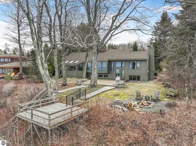 rear view of property with a deck, a fire pit, roof with shingles, and a chimney