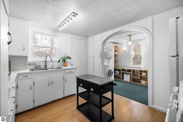 kitchen featuring stacked washing maching and dryer, light wood-type flooring, light countertops, arched walkways, and a sink
