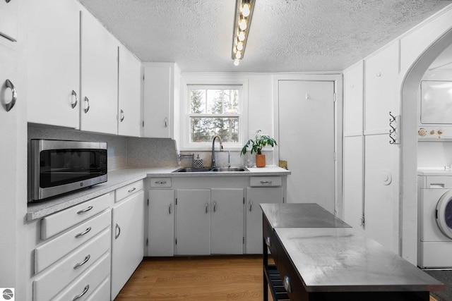 kitchen featuring wood finished floors, light countertops, stainless steel microwave, a sink, and backsplash