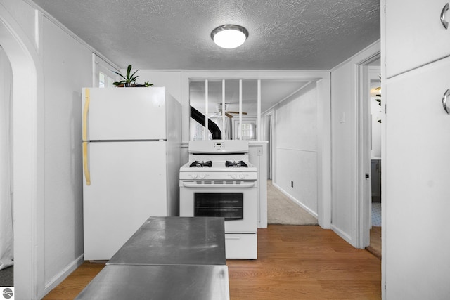 kitchen with arched walkways, a textured ceiling, stainless steel countertops, and white appliances