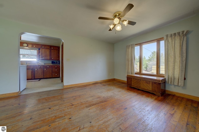 spare room featuring arched walkways, baseboards, plenty of natural light, and light wood-style flooring