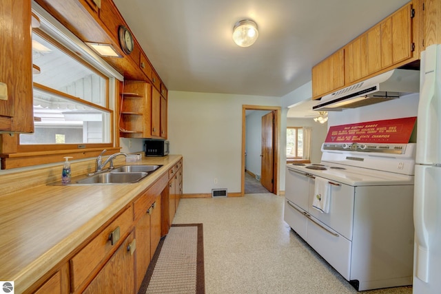 kitchen featuring a sink, white appliances, light countertops, baseboards, and under cabinet range hood