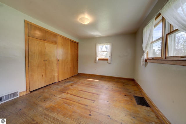 unfurnished bedroom with baseboards, a closet, light wood-style flooring, and visible vents