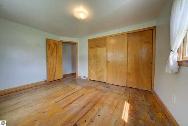 unfurnished bedroom with baseboards, a closet, light wood-style flooring, and visible vents