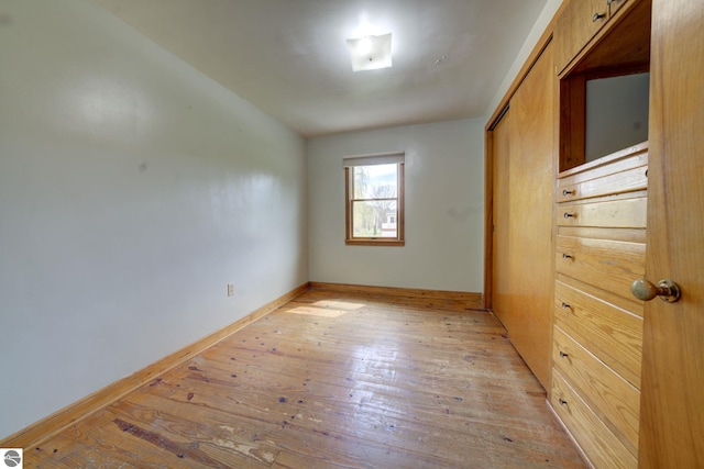 unfurnished bedroom with baseboards, a closet, and light wood-style flooring