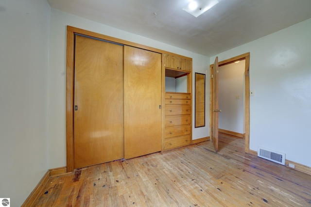 unfurnished bedroom with visible vents, light wood finished floors, baseboards, and a closet