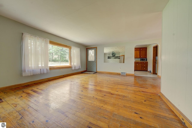unfurnished living room with arched walkways, baseboards, visible vents, and light wood-type flooring