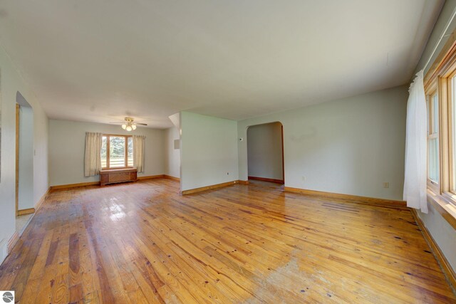 unfurnished room featuring baseboards, arched walkways, light wood finished floors, and a ceiling fan
