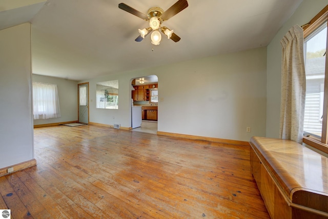 unfurnished living room with a ceiling fan, arched walkways, a healthy amount of sunlight, and hardwood / wood-style flooring