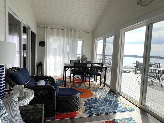 sunroom / solarium with wooden walls, outdoor dining area, wood finished floors, lofted ceiling, and a water view