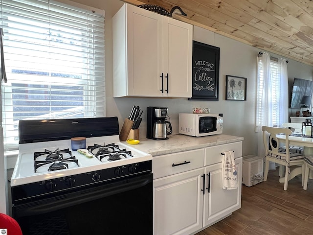 kitchen with white cabinets, dark wood-style flooring, white microwave, and gas range