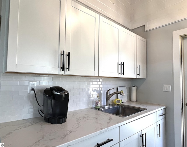 kitchen featuring a sink, white cabinetry, backsplash, and light stone countertops