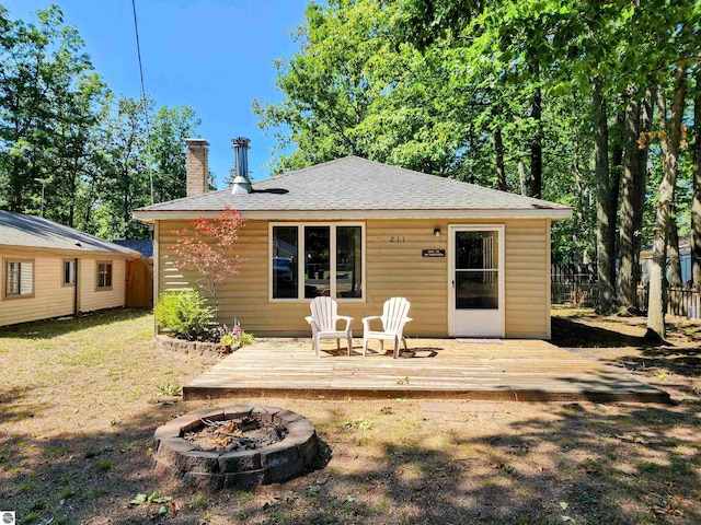 rear view of house featuring a fire pit, fence, a wooden deck, a chimney, and a shingled roof