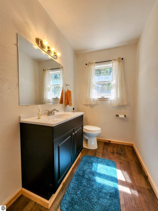bathroom featuring a healthy amount of sunlight, vanity, wood-type flooring, and toilet