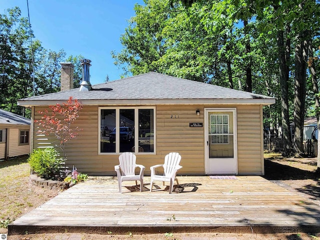 back of house featuring a chimney, a shingled roof, and a deck