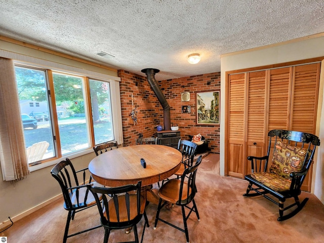 dining area with a textured ceiling, light colored carpet, brick wall, visible vents, and a wood stove