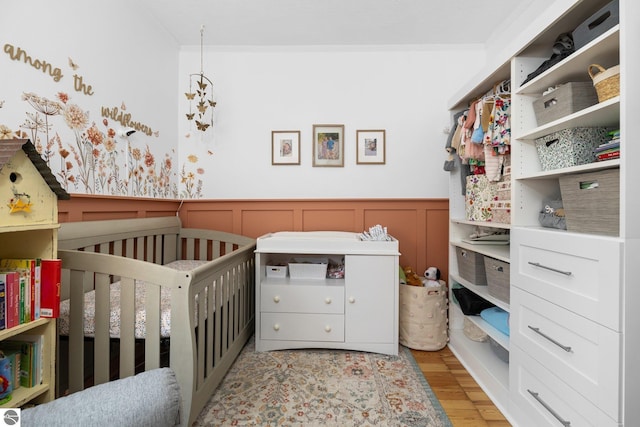 917 Lincoln St, Traverse City, MI 49686 - bedroom with crown molding, a nursery area, wainscoting, a decorative wall, and light wood-style flooring