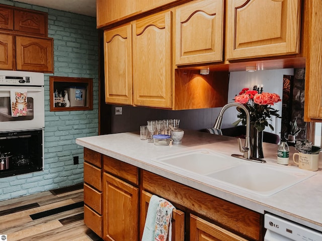 kitchen with a sink, light countertops, white appliances, and light wood-style flooring