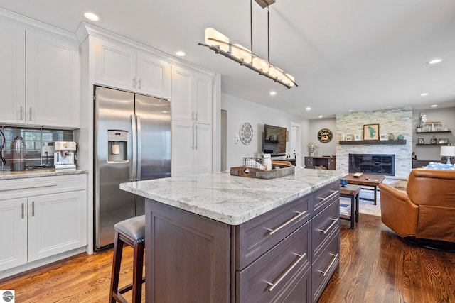 9086 N Tottenham Dr, Traverse City, MI 49685 - kitchen with a stone fireplace, dark wood-style floors, open floor plan, stainless steel fridge, and white cabinetry