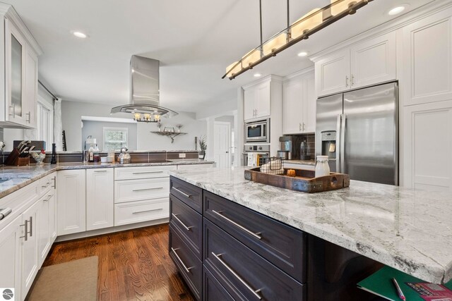 9086 N Tottenham Dr, Traverse City, MI 49685 - kitchen with appliances with stainless steel finishes, white cabinets, dark wood-style floors, and island range hood
